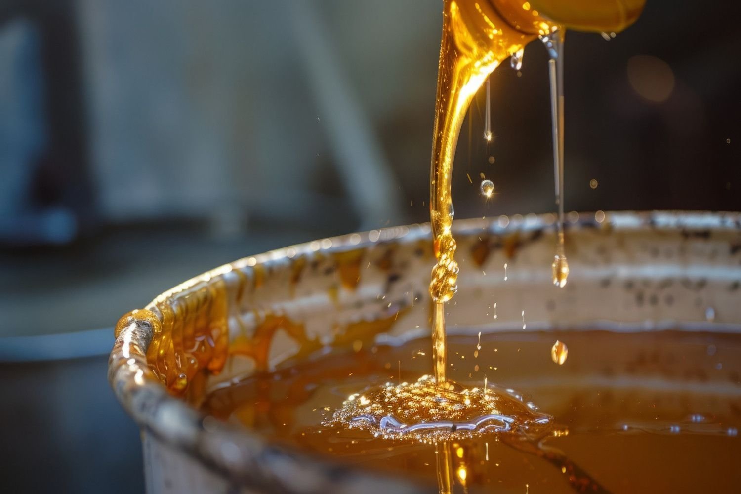 Used oil recycling UAE Saudi: Golden liquid drips from a container, creating splashes in a shiny, reflective surface below.