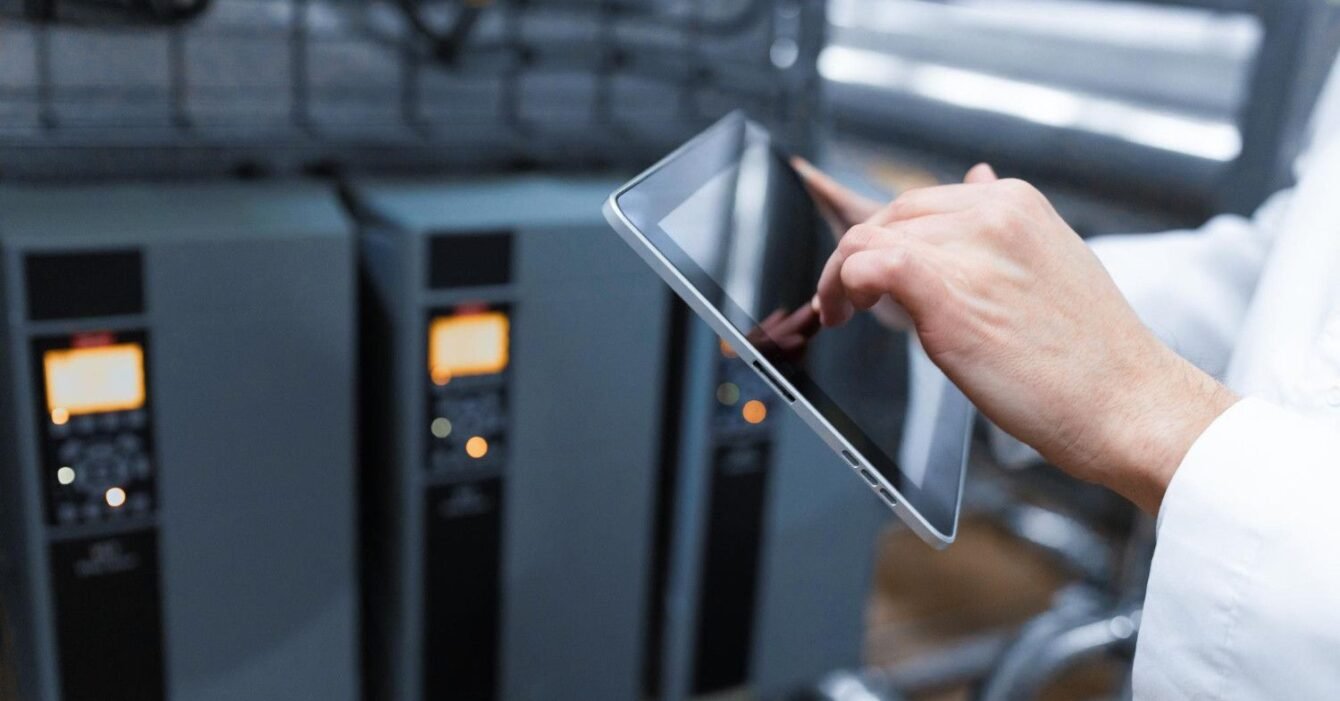 724 data center thermal management: A technician in a white coat uses a tablet to monitor equipment in an industrial setting, with machinery in the background.