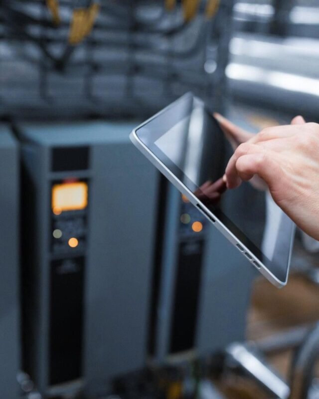 data center thermal management: A technician in a white coat uses a tablet to monitor equipment in an industrial setting, with machinery in the background.