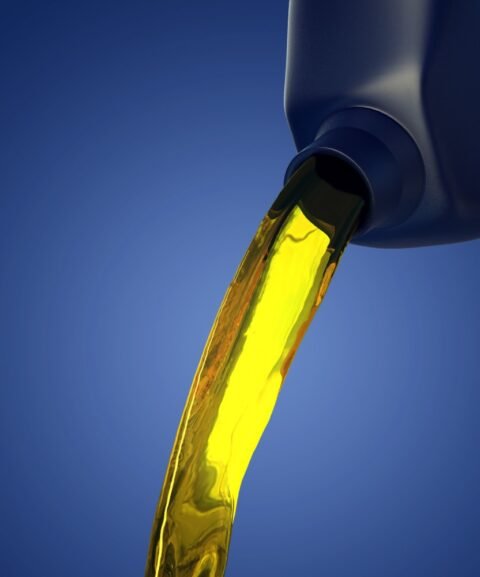 Golden oil flows smoothly from a dark bottle against a vibrant blue background, conveying a sense of purity and precision in motion.