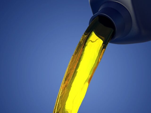 Golden oil flows smoothly from a dark bottle against a vibrant blue background, conveying a sense of purity and precision in motion.