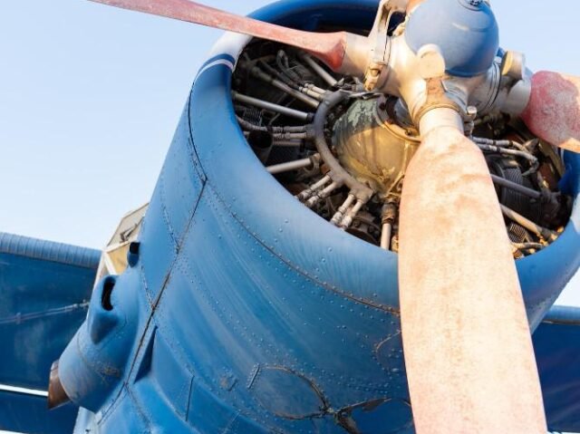 Close-up view of a vintage blue airplane's propeller and engine, set against a clear sky.