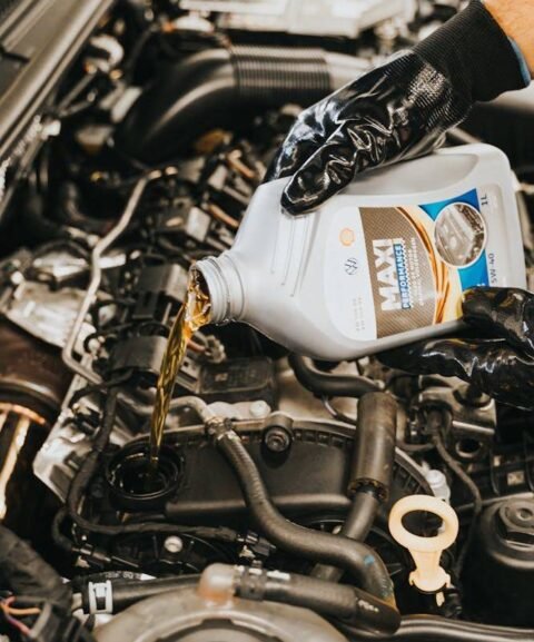 A person wearing black gloves pours motor oil from a container into a car engine.
