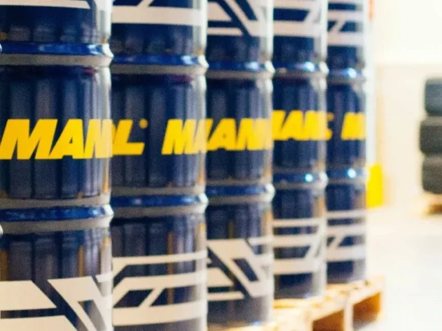 A row of blue industrial barrels with yellow and white branding, neatly arranged on wooden pallets in a warehouse setting.