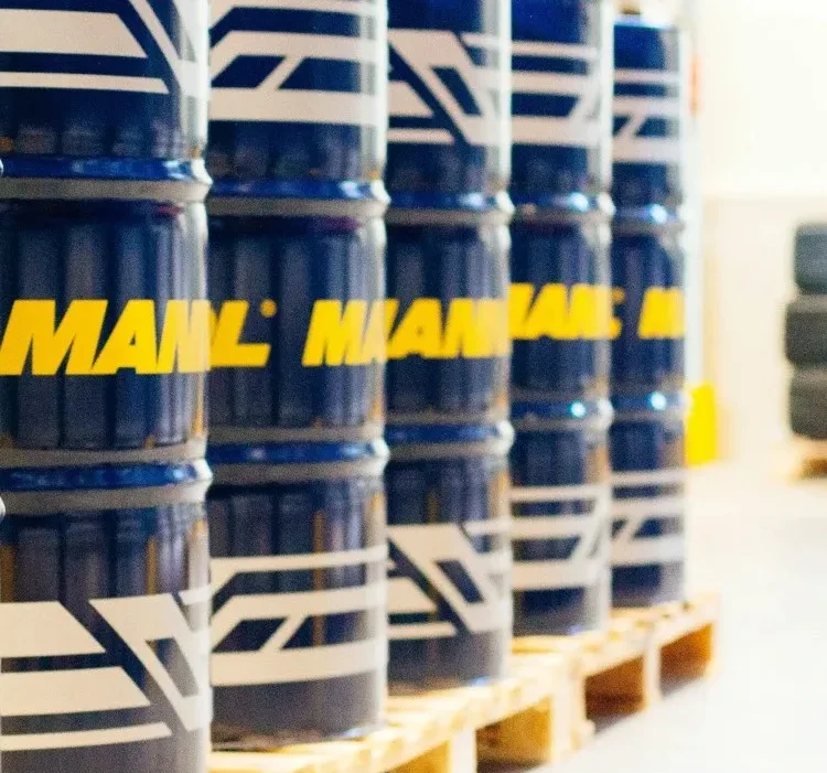 A row of blue industrial barrels with yellow and white branding, neatly arranged on wooden pallets in a warehouse setting.